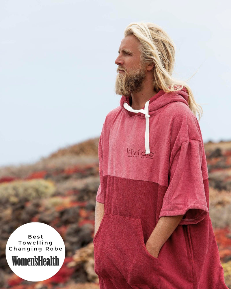 Man wearing a Vivida Original Poncho Towel Changing Robe - Blossom Pink / Rhubarb Red. Sticker reads Women's Health's Best Towelling Changing Robe
