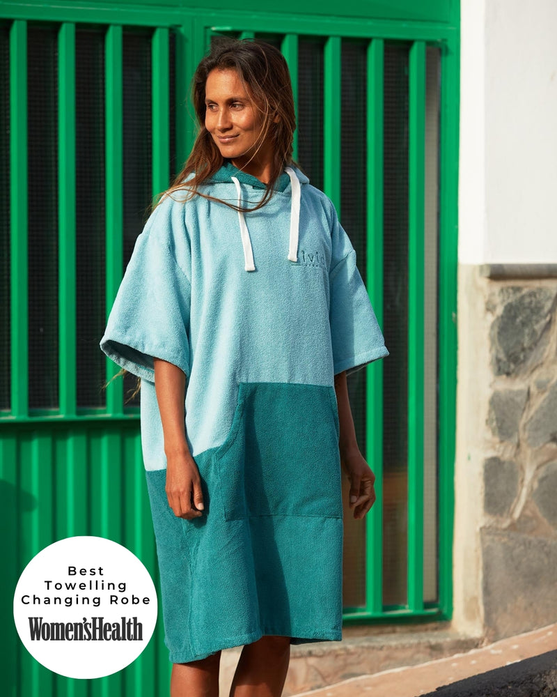 Lead_women - Woman wears a Vivida Original Adult Poncho Towel Changing Robe - Turquoise Teal / Pacific Teal. Sticker reads Women's Health Best Towelling Changing Robe