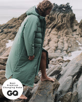 Lead_men - Man wearing a Vivida Lifestyle All Weather Puffer Changing Robe, Aventurine Green Drying Robe for swimming standing on a rock. Sticker: Best Premium Changing Robe - The Independent.