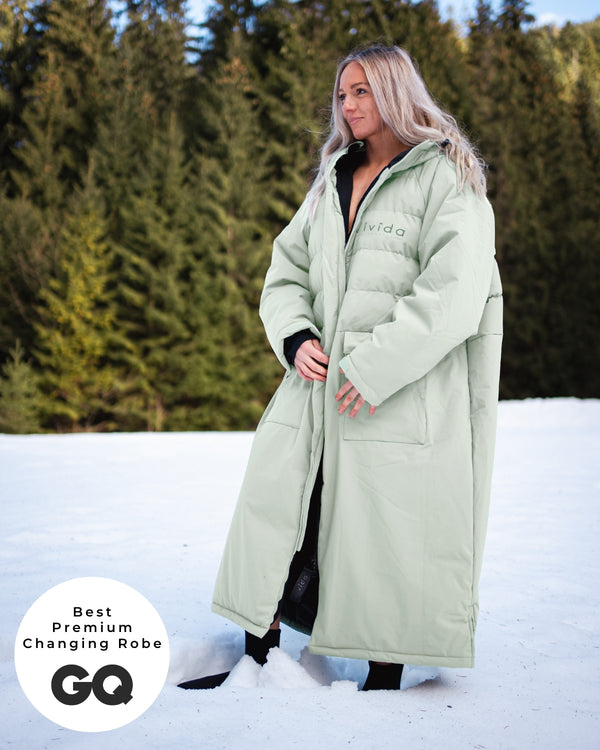 Lead_women - Woman wearing a Vivida Lifestyle All Weather Puffer Changing Robe, Matcha Green Drying Robe for swimming standing in snow. Sticker: Best Premium Changing Robe - The Independent.