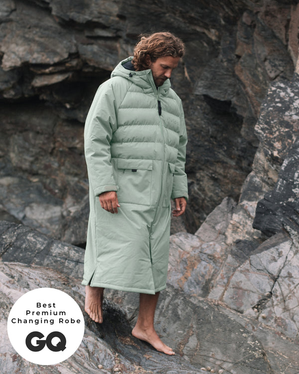 Lead_men - Man wearing a Vivida Lifestyle All Weather Puffer Changing Robe, Matcha Green Drying Robe for swimming standing on rocks. Sticker: Best Premium Changing Robe - The Independent.