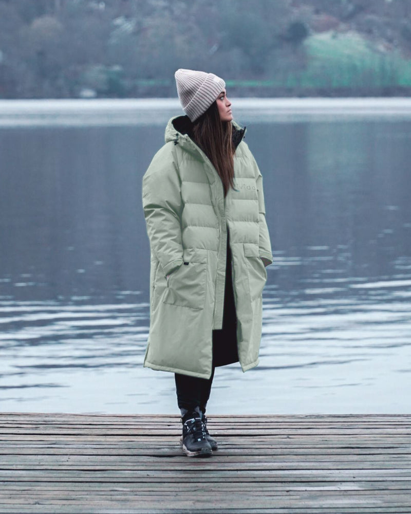 Lead_women2 - Woman wearing a Vivida Lifestyle All Weather Puffer Changing Robe, Matcha Green Drying Robe for swimming standing in snow. Sticker: Best Premium Changing Robe - The Independent.