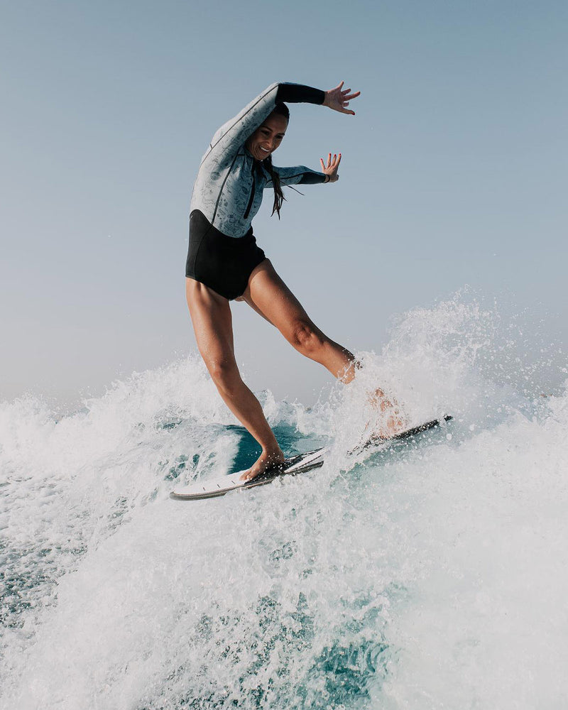 Woman wearing a Vivida Linda Reversible Shortie Neoprene Wetsuit - Graphite / Map of Dreams surfing