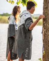 A woman and a man wearing the Vivida Premium Poncho Towel Changing Robe - Cloud Blue Map of Dreams