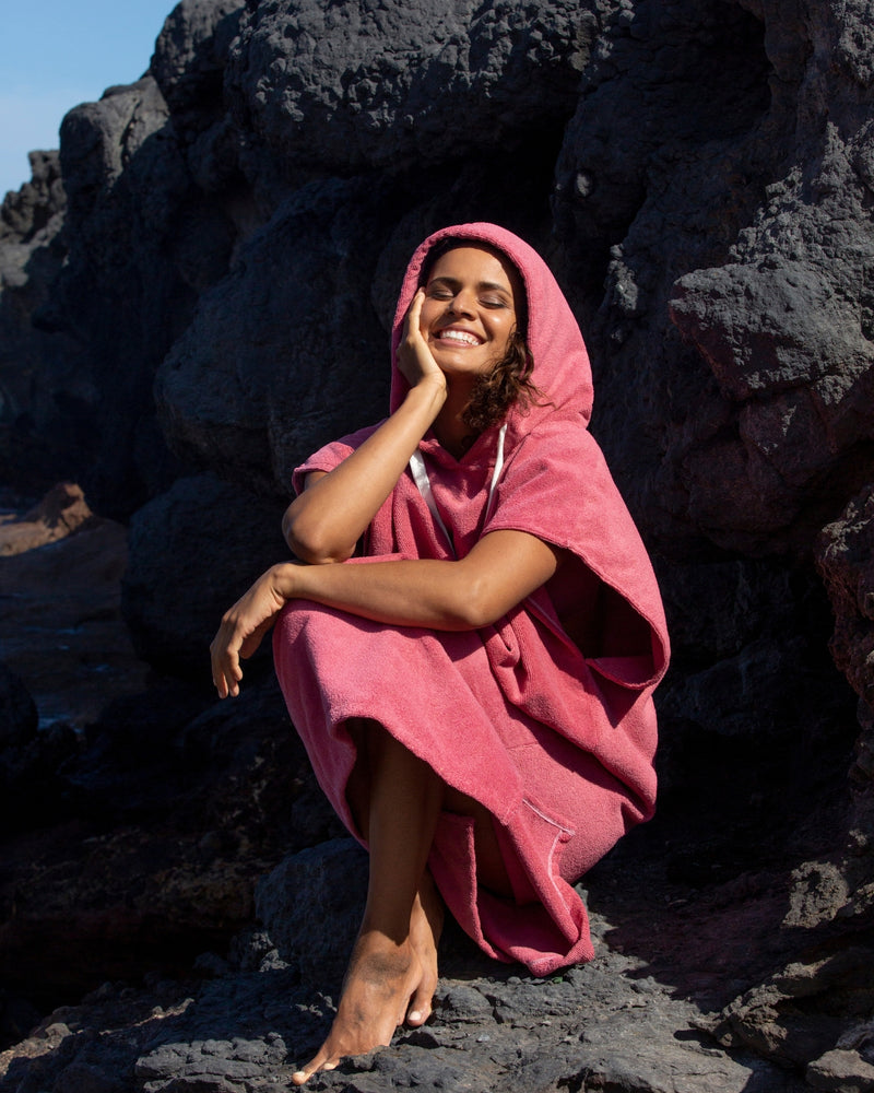 Woman sitting on beach in a Vivida Essential Poncho Towel Pink