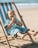 Baby sitting on beach chair eating an ice cream wearing a green poncho towel for toddlers