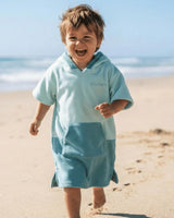 Lead_men Child wearing a light green poncho towel with 'Vivida' branding on a sandy beach.