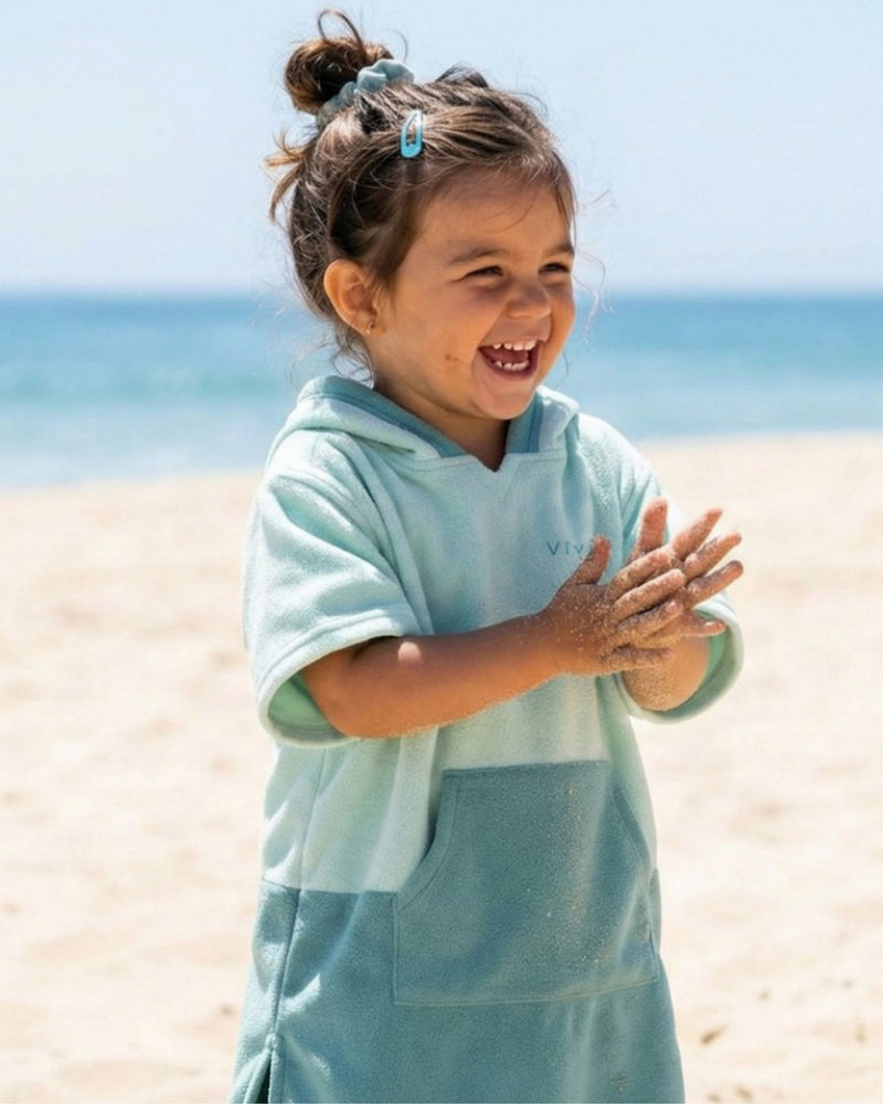 Baby toddler laughing on the beach wearing a poncho beach towel in colours green and teal 