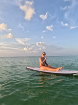 Woman doing yoga on a standup paddleboard wearing Vivida Women of the sea rashguard and Nefeli bikini bottoms